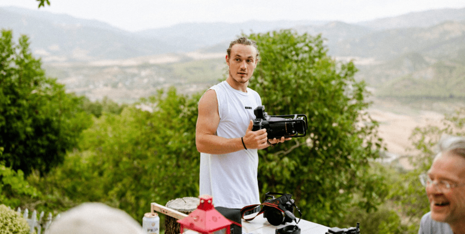 Alt Tag: Fotograf Leander im weißen Shirt und einer Kamera draußen in der Natur